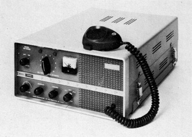 Radio transceiver with 6 knobs and a meter on the ront and a microphone on the top.