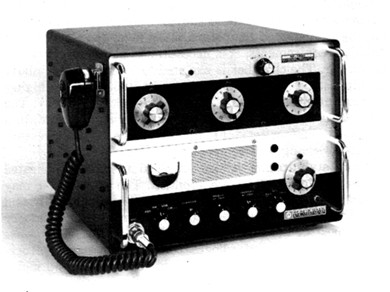Radio transceiver with 10 knobs, meter and speaker grill on front and microphone hung on left side.