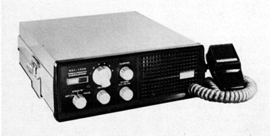 Radio transceiver with 5 knobs on front and microphone beside unit on right side.