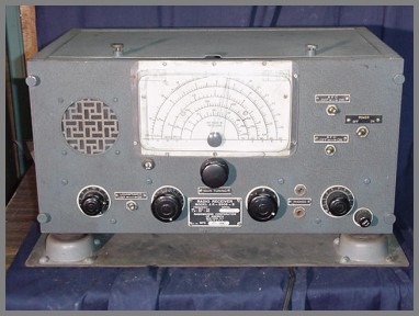 Shock-mounted radio receiver with 4 knobs, a tuning knob, speaker grill and a semi-circular dial