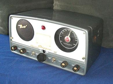 Tabletop radio transceiver with a big round speaker grill on left front and a round dial on the right and 5 knobs and 2 toggle switches below.