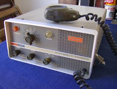 Tabletop Radio transceiver with 1 big knob, 3 small knobs and speaker grill on right front and microphone on top.